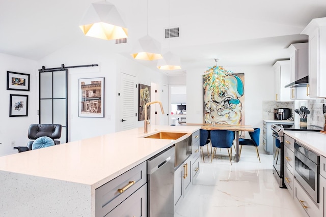 kitchen featuring stainless steel appliances, decorative light fixtures, a barn door, vaulted ceiling, and an island with sink