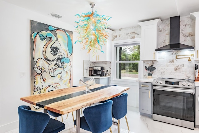 kitchen featuring white cabinets, wall chimney range hood, electric range, backsplash, and pendant lighting