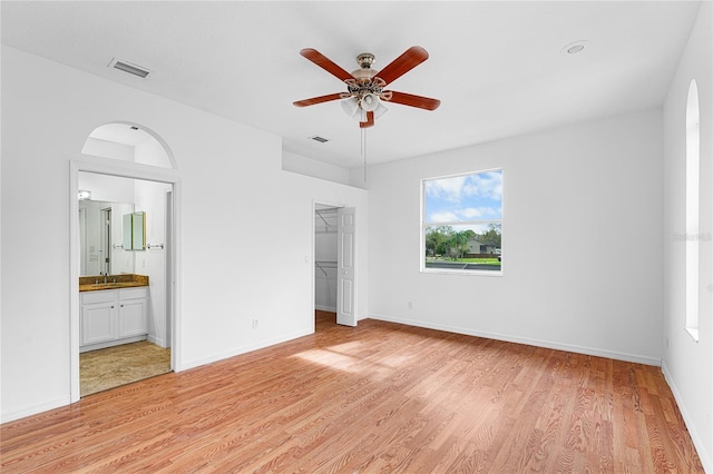 unfurnished bedroom with ceiling fan, a spacious closet, connected bathroom, light hardwood / wood-style floors, and a closet