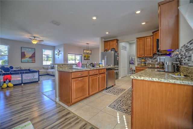 kitchen with ceiling fan with notable chandelier, stainless steel appliances, decorative light fixtures, light stone countertops, and light hardwood / wood-style flooring