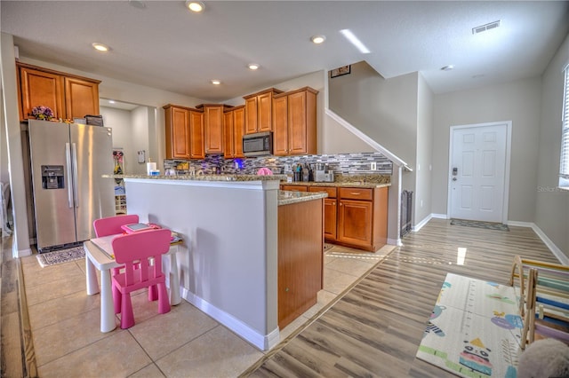 kitchen with stainless steel appliances, light stone counters, a center island, tasteful backsplash, and light wood-type flooring