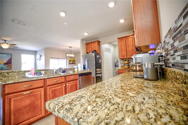 kitchen featuring stainless steel appliances, backsplash, pendant lighting, light stone countertops, and ceiling fan with notable chandelier