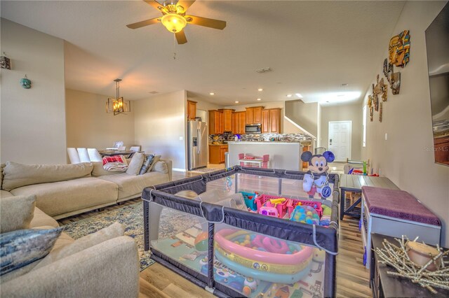 living room featuring ceiling fan with notable chandelier and light hardwood / wood-style floors