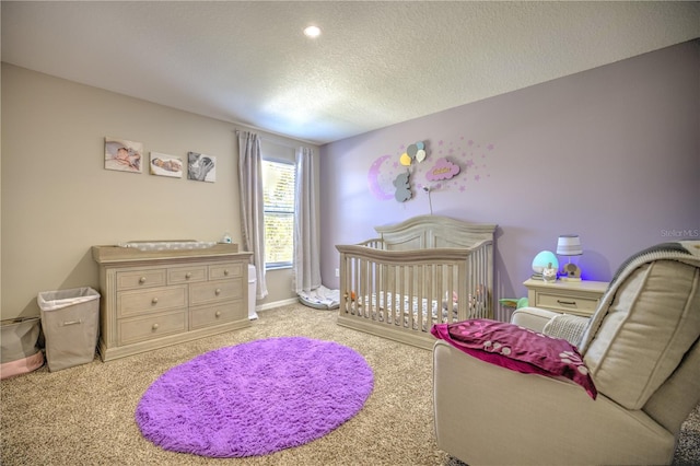 bedroom featuring a crib, light colored carpet, and a textured ceiling