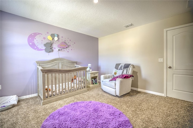 carpeted bedroom featuring a nursery area and a textured ceiling