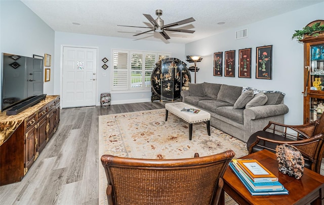 living room featuring ceiling fan, light wood-type flooring, and a textured ceiling