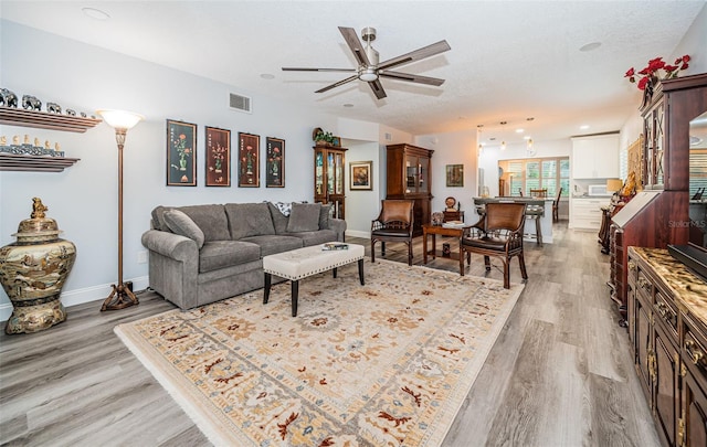 living room with ceiling fan, light hardwood / wood-style floors, and a textured ceiling