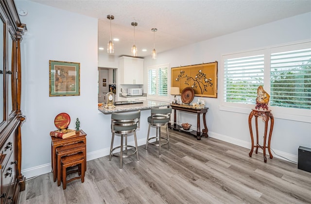 kitchen featuring light stone countertops, hanging light fixtures, light hardwood / wood-style floors, a kitchen bar, and white cabinets