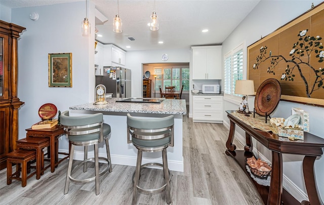 kitchen featuring light stone countertops, stainless steel fridge, light hardwood / wood-style flooring, white cabinets, and hanging light fixtures