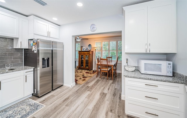 kitchen with stainless steel fridge, white cabinets, light hardwood / wood-style floors, and light stone counters