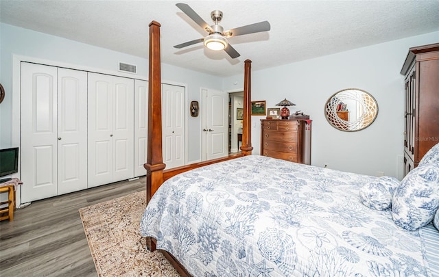 bedroom with two closets, ceiling fan, a textured ceiling, and hardwood / wood-style flooring