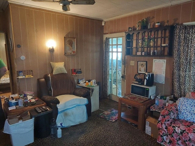 sitting room with ornamental molding, wood walls, and ceiling fan