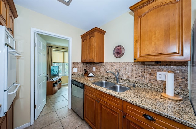 kitchen with dishwasher, light stone counters, brown cabinetry, and a sink