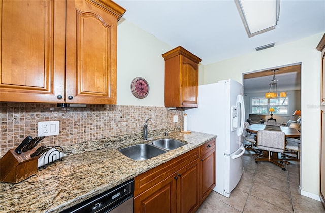 kitchen with light stone counters, white refrigerator with ice dispenser, decorative backsplash, sink, and dishwashing machine