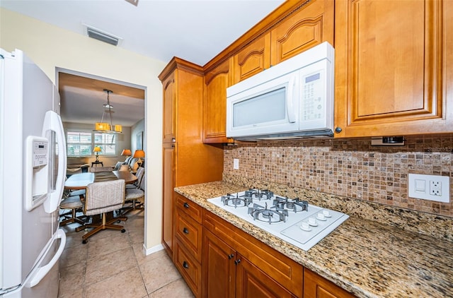 kitchen with tasteful backsplash, light stone counters, decorative light fixtures, light tile patterned floors, and white appliances