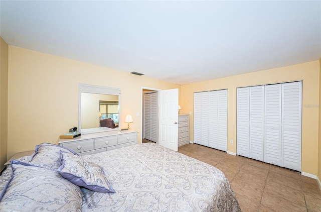 bedroom featuring baseboards, light tile patterned floors, visible vents, and multiple closets