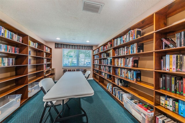 office area featuring wall of books, visible vents, dark colored carpet, and a textured ceiling