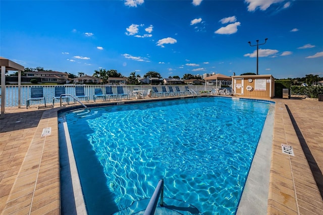 view of swimming pool featuring a patio, an outdoor structure, and a water view