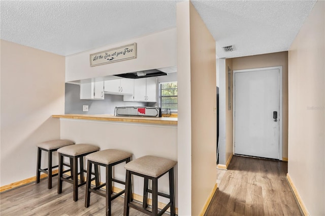 kitchen featuring white cabinets, kitchen peninsula, a textured ceiling, a breakfast bar area, and light wood-type flooring