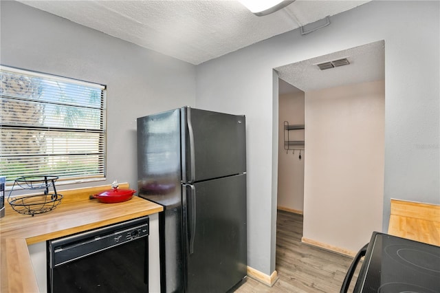 kitchen featuring light wood-type flooring, wood counters, a textured ceiling, and black appliances