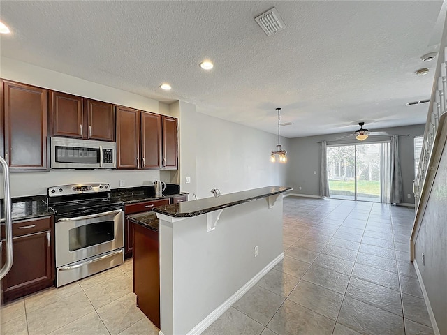 kitchen featuring appliances with stainless steel finishes, decorative light fixtures, light tile patterned floors, a kitchen breakfast bar, and a center island