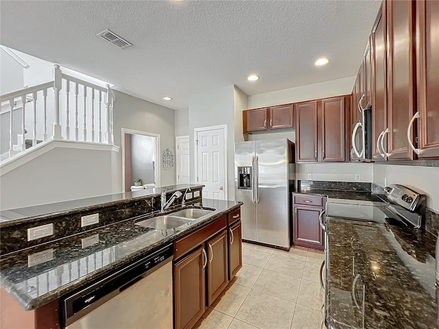 kitchen with a textured ceiling, stainless steel appliances, dark stone counters, and sink