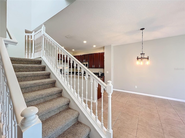 stairs with a textured ceiling, tile patterned floors, and an inviting chandelier