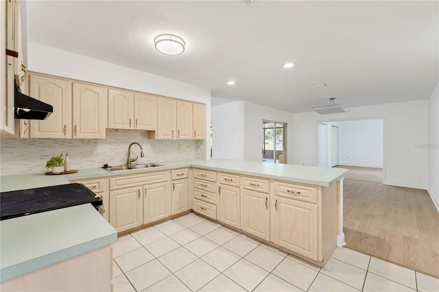 kitchen with range, decorative backsplash, sink, kitchen peninsula, and light hardwood / wood-style flooring