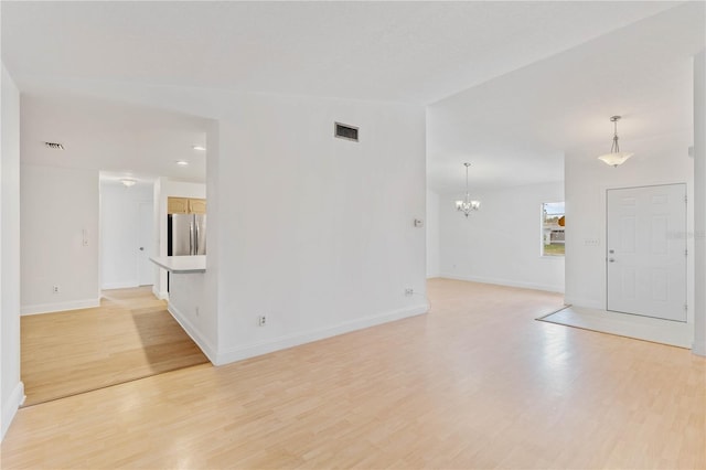 spare room featuring a chandelier and light hardwood / wood-style floors