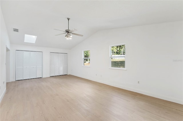 unfurnished bedroom with light wood-type flooring, multiple closets, ceiling fan, and vaulted ceiling with skylight