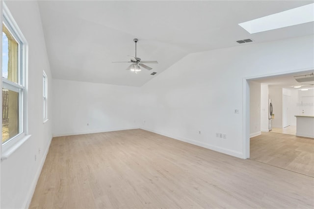 empty room featuring lofted ceiling with skylight, light wood-type flooring, and a healthy amount of sunlight