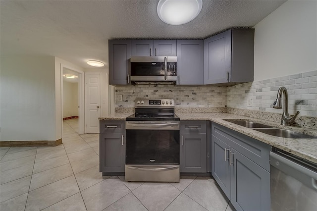 kitchen with a textured ceiling, sink, gray cabinets, light stone countertops, and appliances with stainless steel finishes