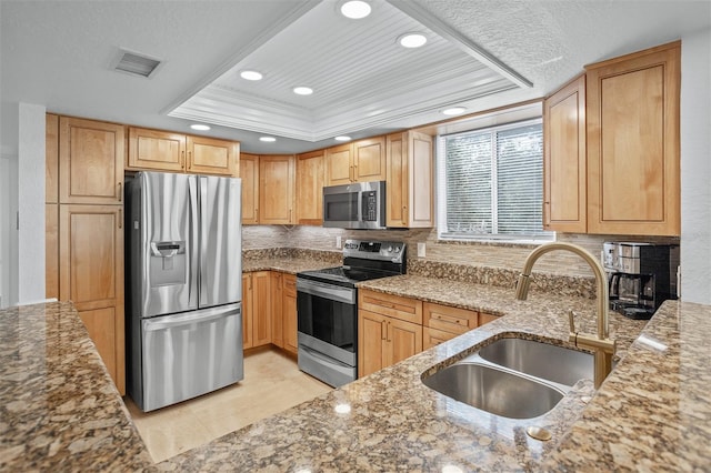 kitchen with stainless steel appliances, sink, ornamental molding, a raised ceiling, and light stone countertops