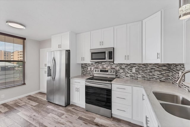 kitchen featuring stainless steel appliances, white cabinets, sink, backsplash, and light wood-type flooring