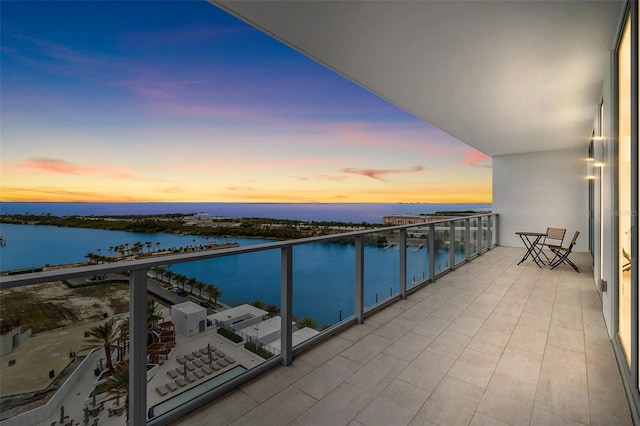 balcony at dusk featuring a water view