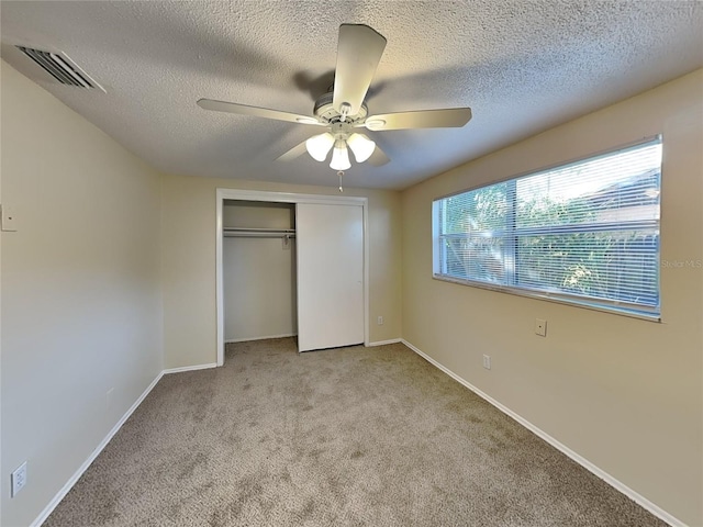 unfurnished bedroom with ceiling fan, light carpet, a closet, and a textured ceiling