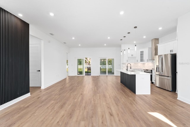 kitchen featuring stainless steel appliances, white cabinets, a center island with sink, wall chimney range hood, and pendant lighting