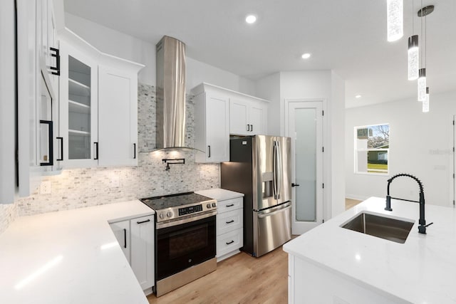 kitchen featuring wall chimney exhaust hood, decorative light fixtures, white cabinetry, appliances with stainless steel finishes, and sink