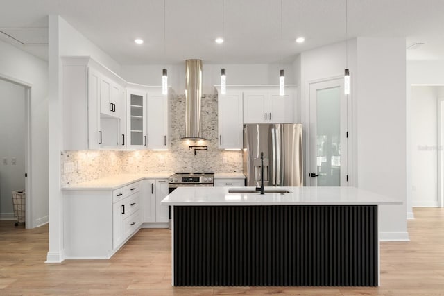 kitchen with stainless steel appliances, decorative light fixtures, backsplash, a center island with sink, and wall chimney range hood