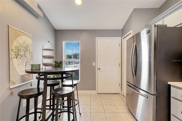 kitchen featuring light tile patterned flooring, stainless steel refrigerator, and a kitchen bar