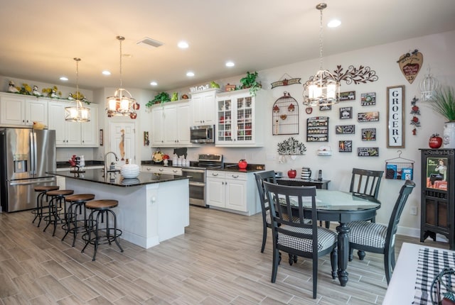 kitchen with white cabinetry, decorative light fixtures, an island with sink, and stainless steel appliances