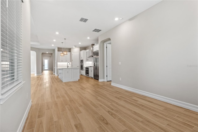 unfurnished living room featuring sink, light hardwood / wood-style floors, and a notable chandelier