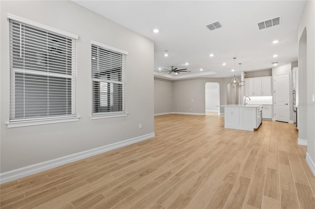 unfurnished living room featuring ceiling fan with notable chandelier, light hardwood / wood-style flooring, and sink