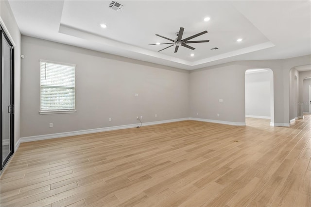 empty room featuring ceiling fan, light hardwood / wood-style floors, and a tray ceiling