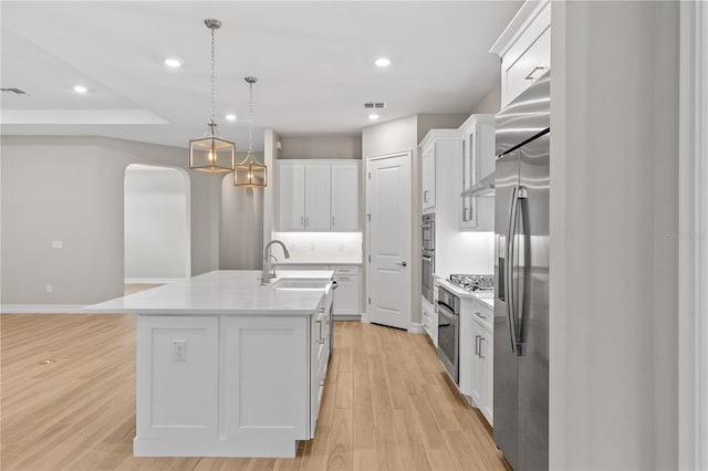 kitchen featuring sink, hanging light fixtures, an island with sink, white cabinets, and light wood-type flooring