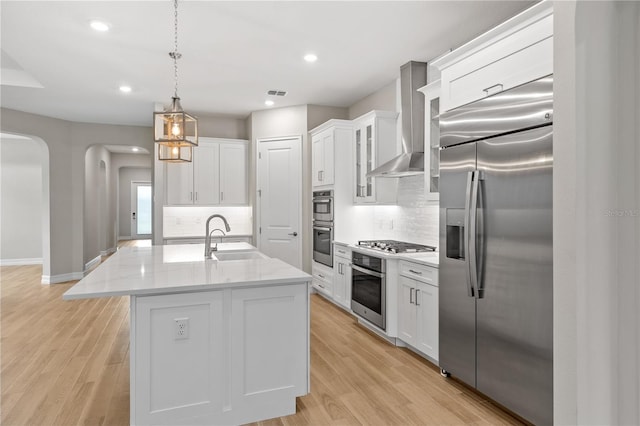 kitchen with pendant lighting, wall chimney range hood, sink, appliances with stainless steel finishes, and white cabinetry