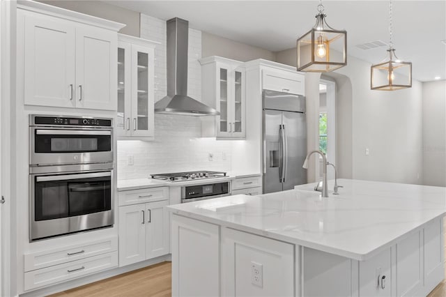 kitchen with white cabinets, wall chimney exhaust hood, stainless steel appliances, and decorative light fixtures