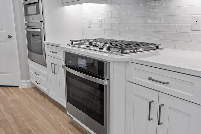 kitchen featuring decorative backsplash, white cabinetry, stainless steel appliances, and light hardwood / wood-style flooring