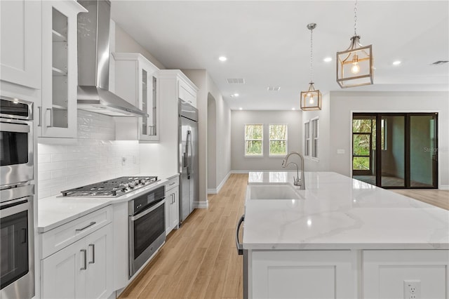 kitchen with decorative light fixtures, white cabinetry, wall chimney range hood, and sink