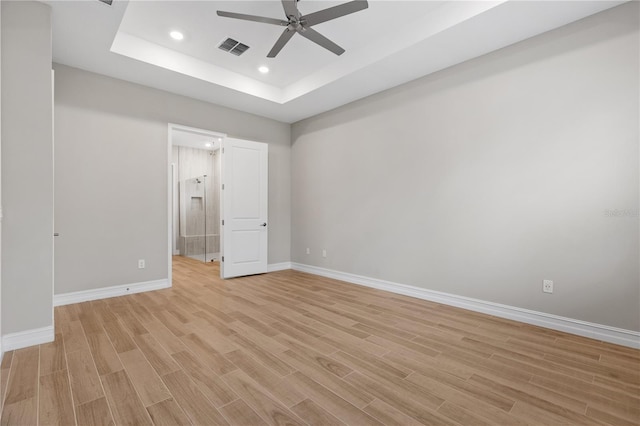 unfurnished bedroom with light hardwood / wood-style floors, ceiling fan, and a tray ceiling